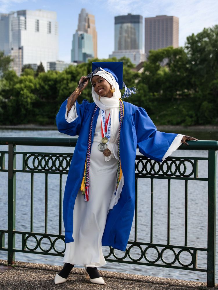 Graduate in a blue gown by the river with the skyline
