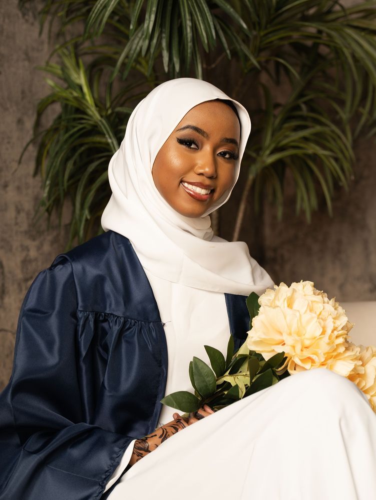 Graduate in a white hijab and navy gown holding flowers