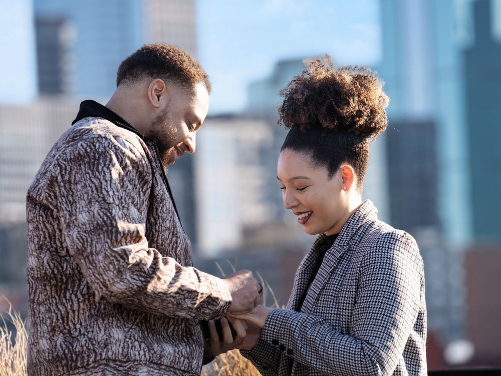 He slides the ring onto her finger with the city behind them