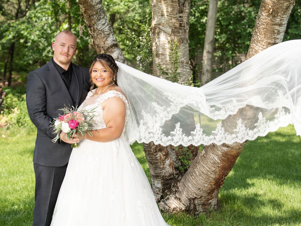 Bride's veil lifting in the wind as the couple poses by a birch tree